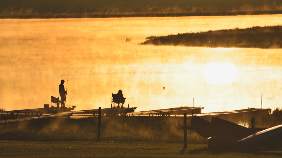 Early morning fishermen over a golden lake with the mist rising. by Jax Facts a couple of people standing on top of a boat