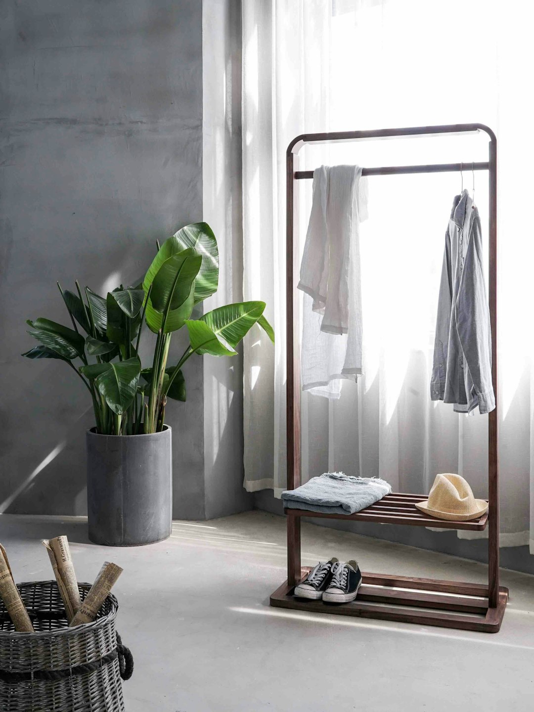Tidy minimal interior by Jax Facts gray dress shirt hang on brown wooden rack in front of window with white curtain